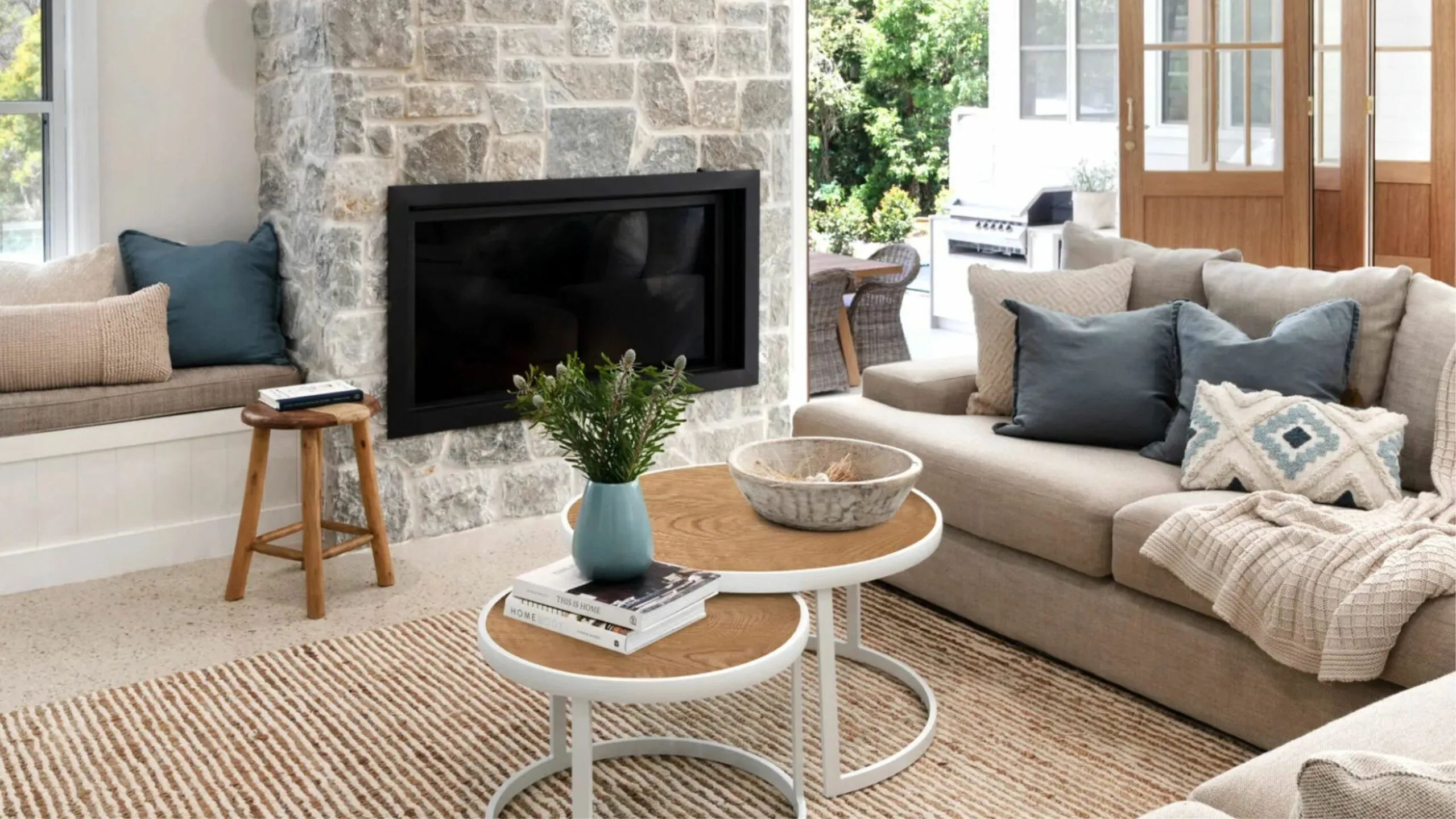 Cozy living room with a stone fireplace, beige sofa, blue cushions, and a round coffee table with decor.