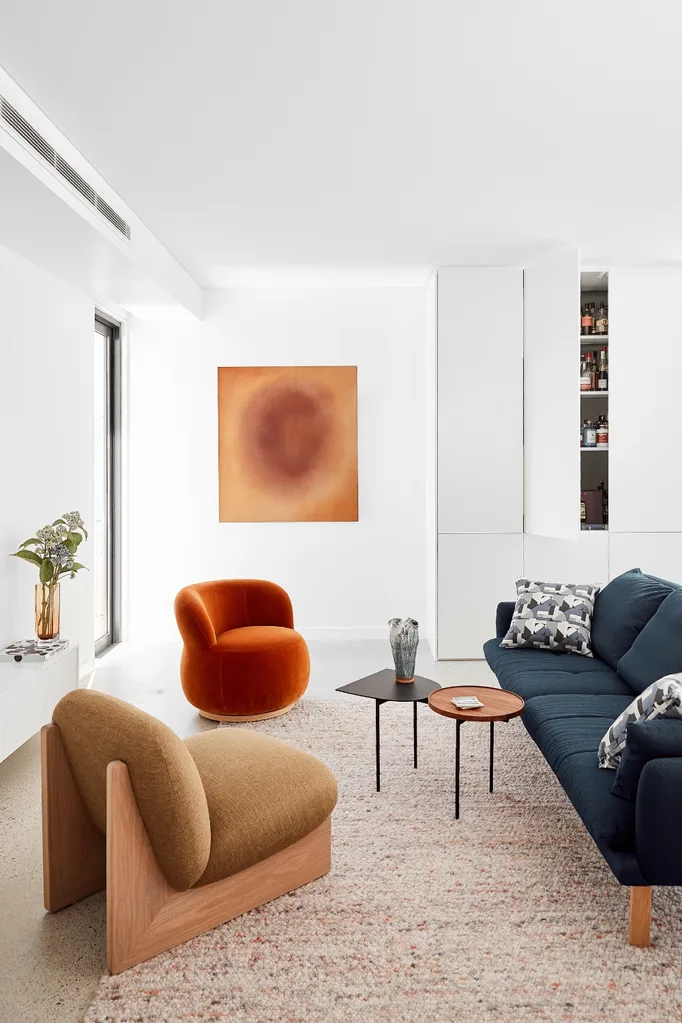 Modern living room with orange and beige chairs, blue sofa, and abstract art on white wall.
