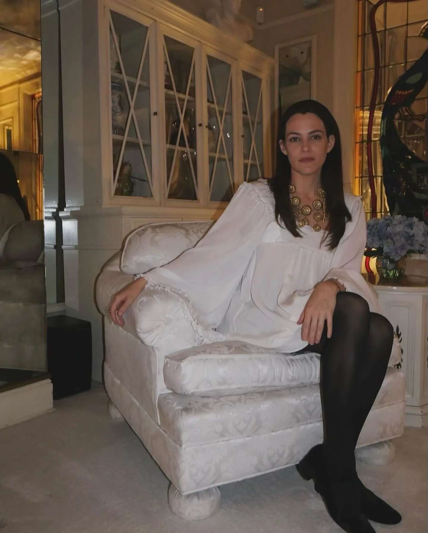 Riley Keough sitting on a white couch in Graceland's living room.