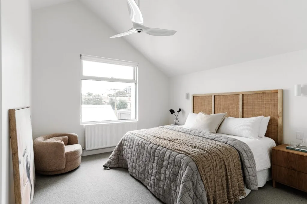 White bedroom with vaulted ceiling fan and rattan bedhead.