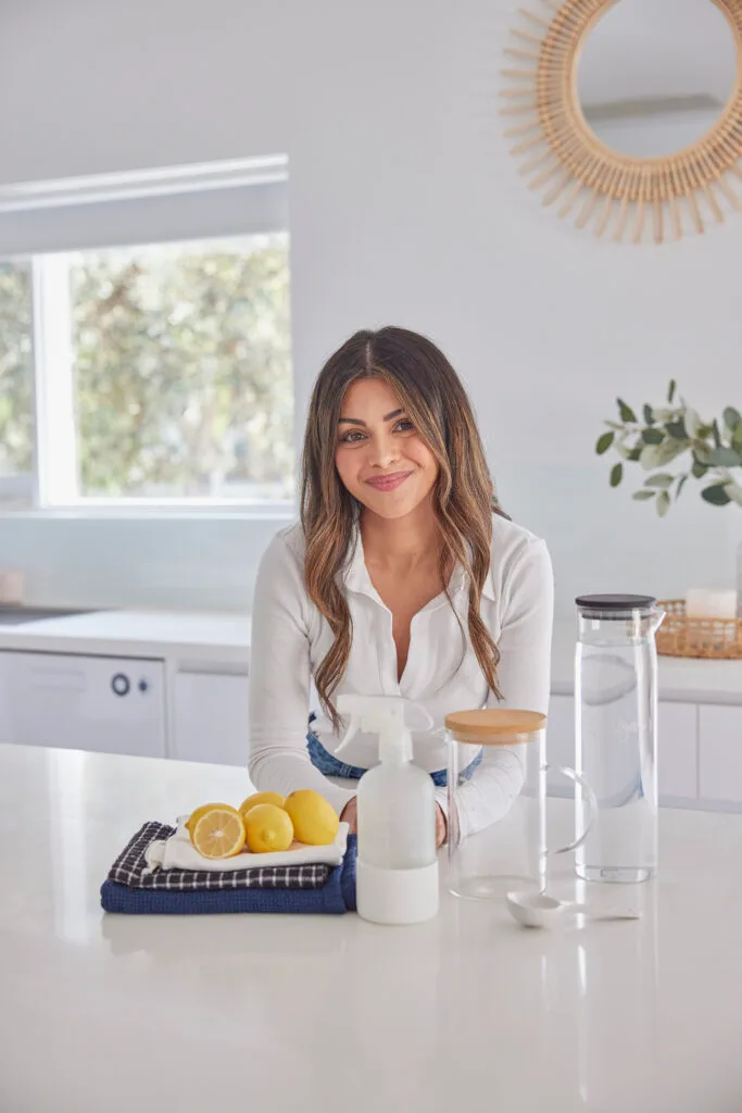 Chantel Mila Ibbotson, cleaning guru and author pictured in a white kitchen with natural cleaning products.