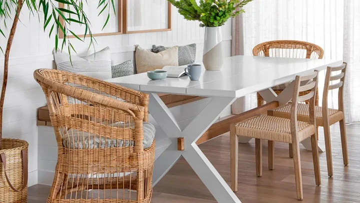 Bright dining area with a white table, wicker chairs, and green plant decor.