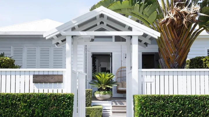 White coastal house entrance with a garden, palm tree, and a hanging chair.