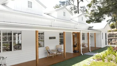 Modern white farmhouse with timber deck and dormer windows.