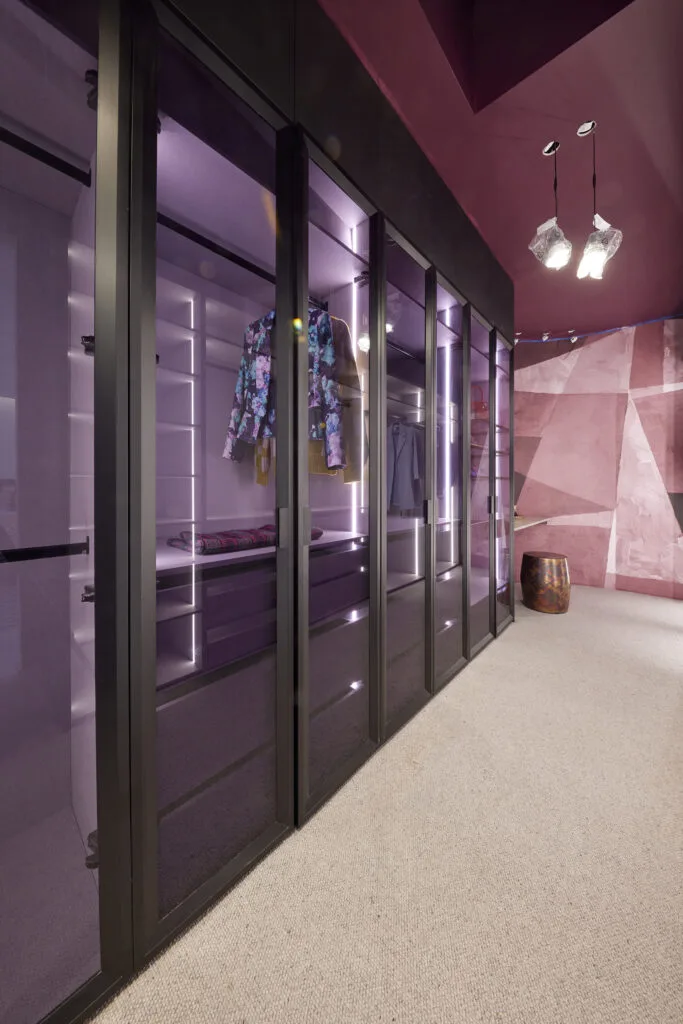 Walk in wardrobe with plum and purple walls and glass doors.