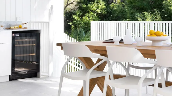 Outdoor dining area with wooden table, white chairs, and lemons on a platter. A small fridge is visible under the counter.
