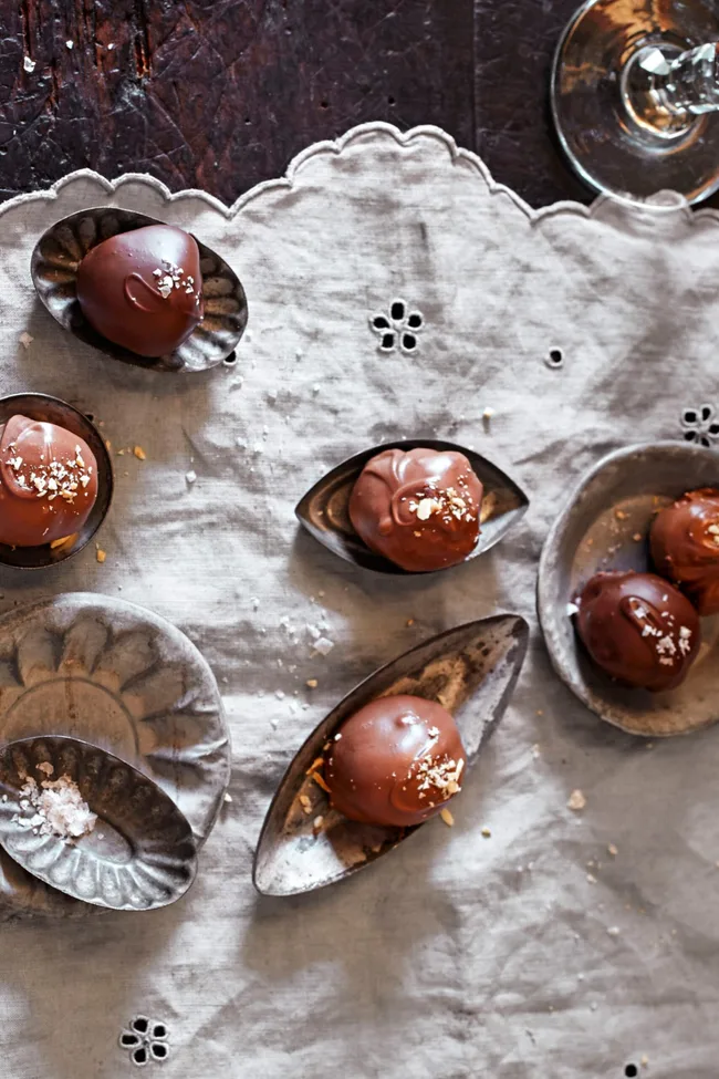 Chocolate truffles with sea salt on decorative metal trays on a lace tablecloth.