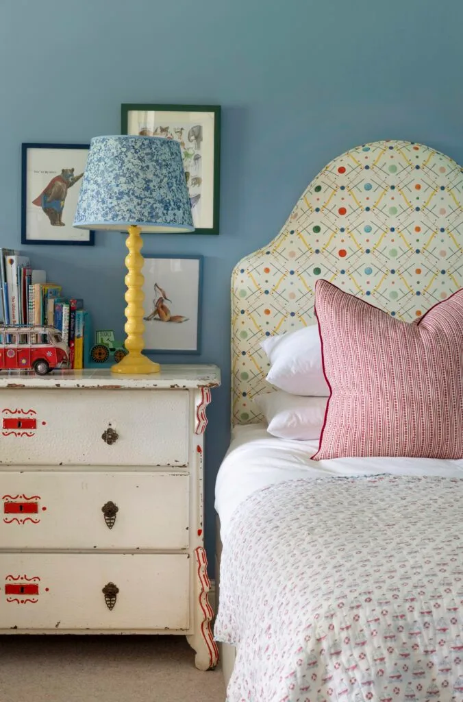 Children's bedroom with blue walls and bright patterned bed.