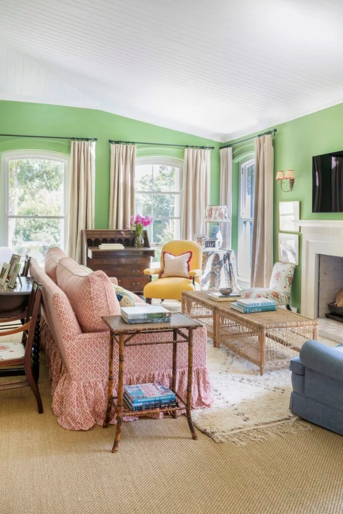 A classical English living room with eclectic green walls and bright red patterned sofa.