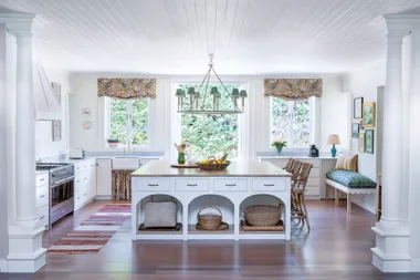 White classical English kitchen with square island and patterned curtains.