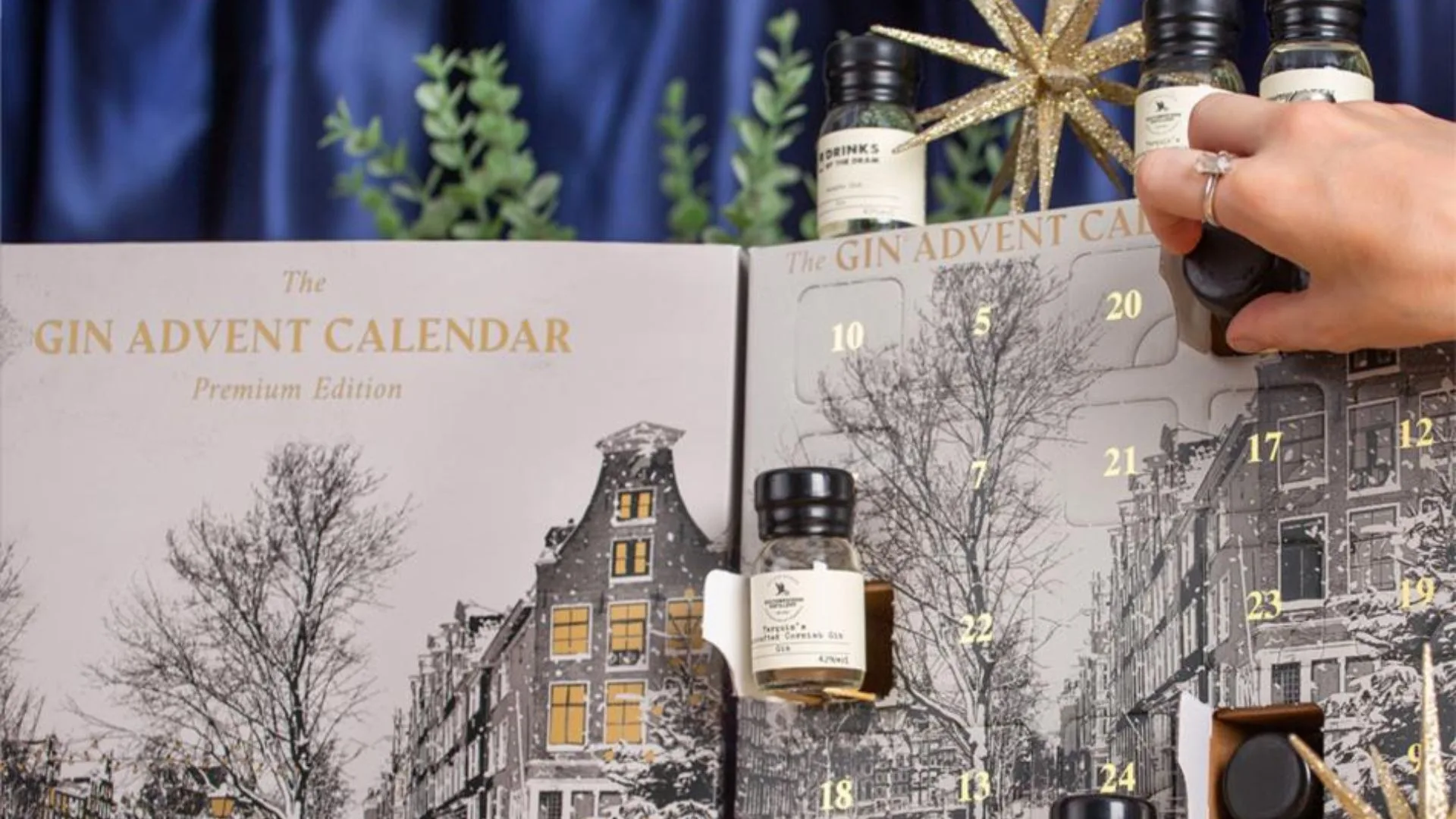 Hand opening a day on a "Gin Advent Calendar Premium Edition," revealing a small bottle of gin.