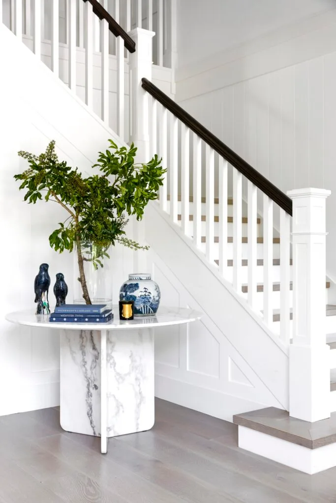 All-white foyer with marble table and staircase.