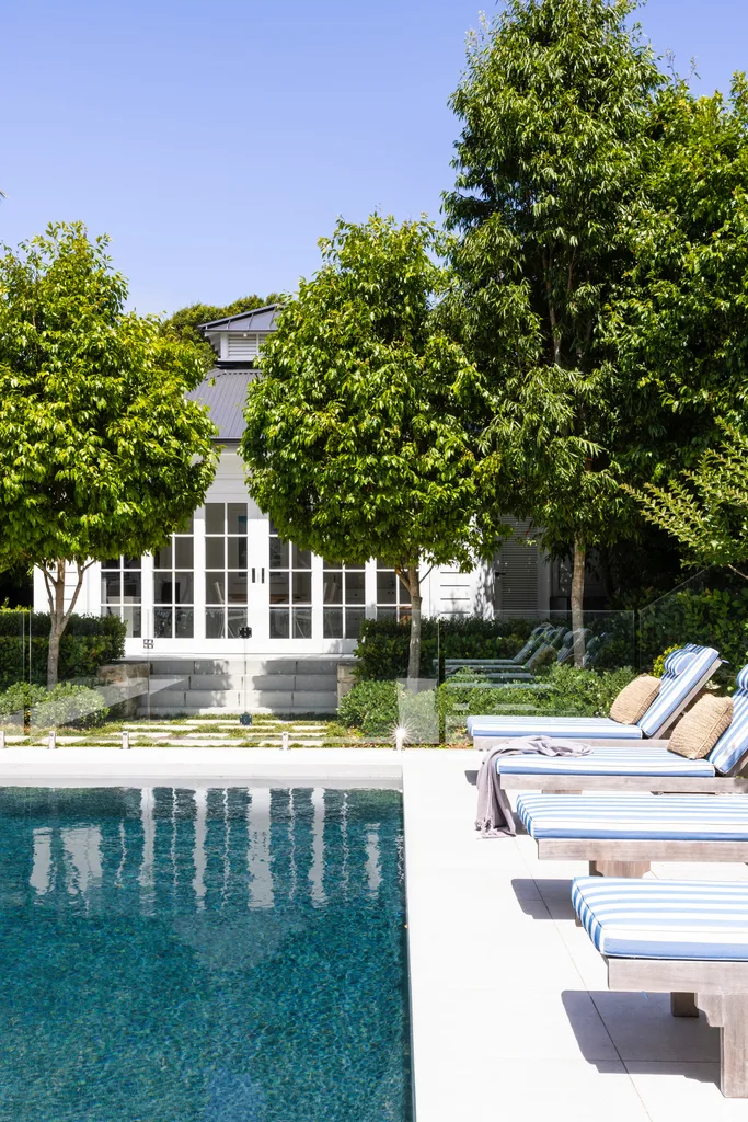 Hamptons style pool and pool house with striped blue chairs.