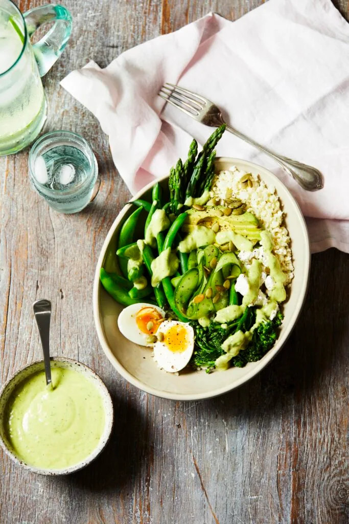 A healthy green breakfast bowl with asparagus and eggs with dressing.