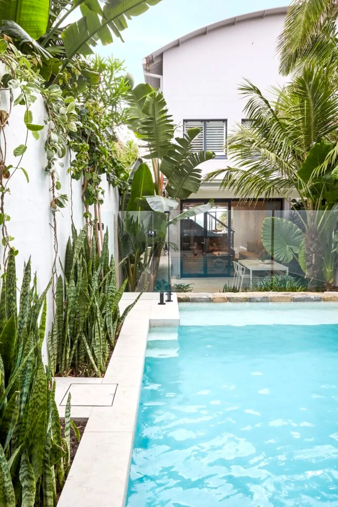 Pool surrounded and tropical plants by outdoor entertaining area.