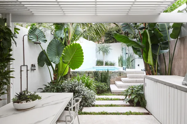 Outdoor kitchen and dining area with pool and palms.