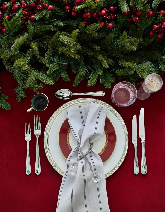 Red tablecloth with green garland centrepiece and white and silver tableware for traditional Christmas table decorations