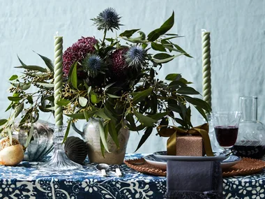 A blue tablecloth with a large vase of flowers on top and two spiral candlesticks
