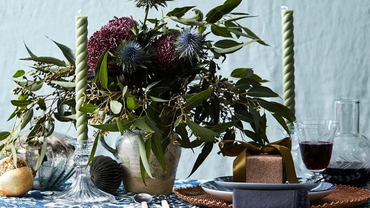 A blue tablecloth with a large vase of flowers on top and two spiral candlesticks