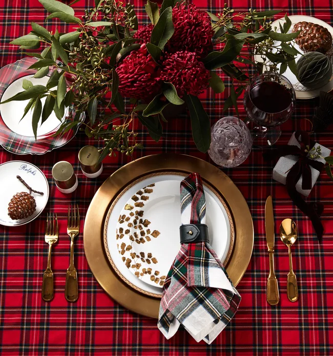 A plaid tablecloth with plaid napkin and red native plants as a centrepiece
