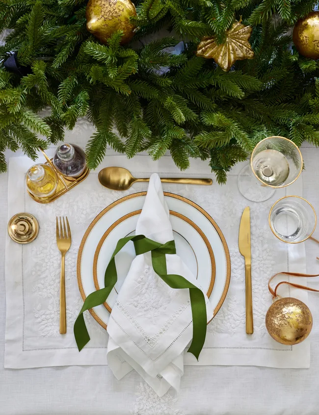 Christmas table decorations with white table linen, green garland and gold cutlery