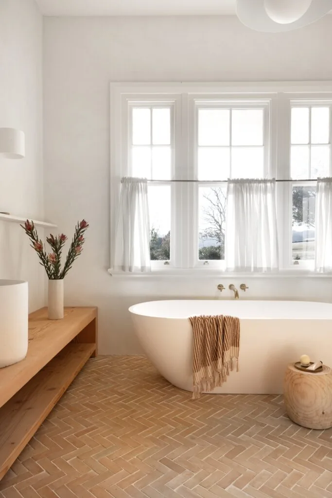 A modern country bathroom in white with terracotta tiles and a freestanding tub.