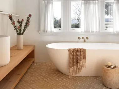 A modern country bathroom in white with terracotta tiles and a freestanding tub.
