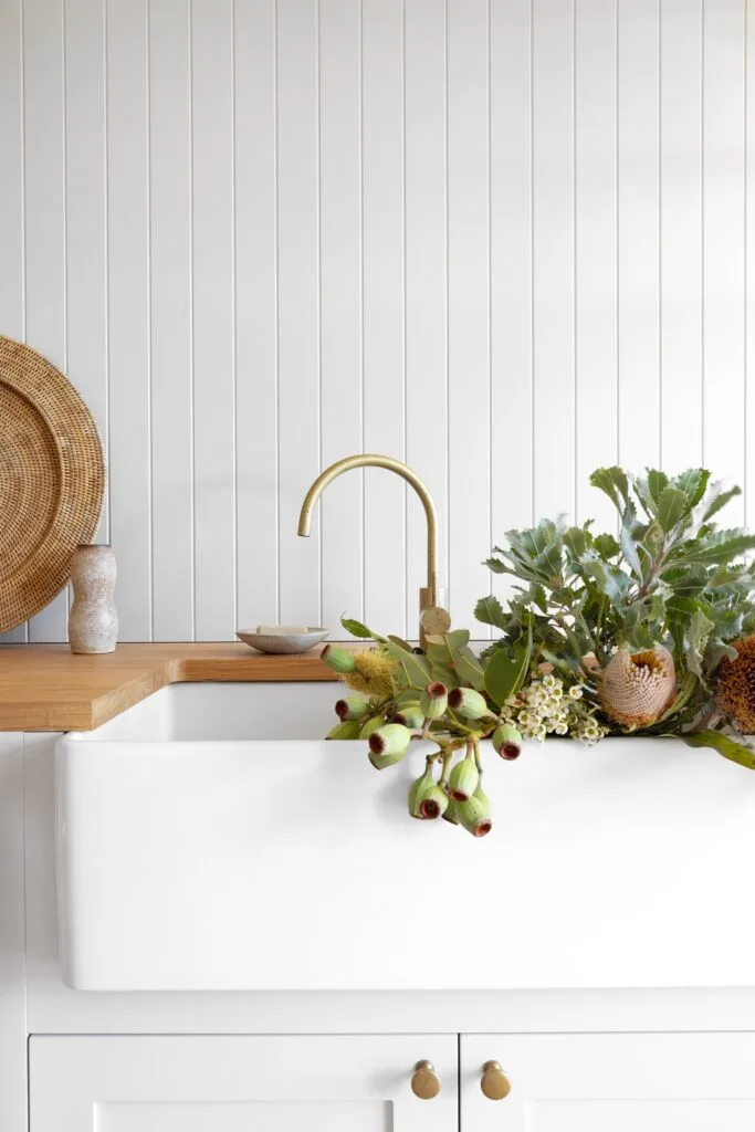 An all-white laundry with panelled walls and a timber benchtop.