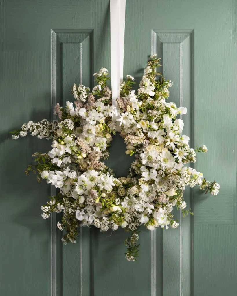 A white Christmas wreath with flannel flowers, lily of the valley and sweet pea.