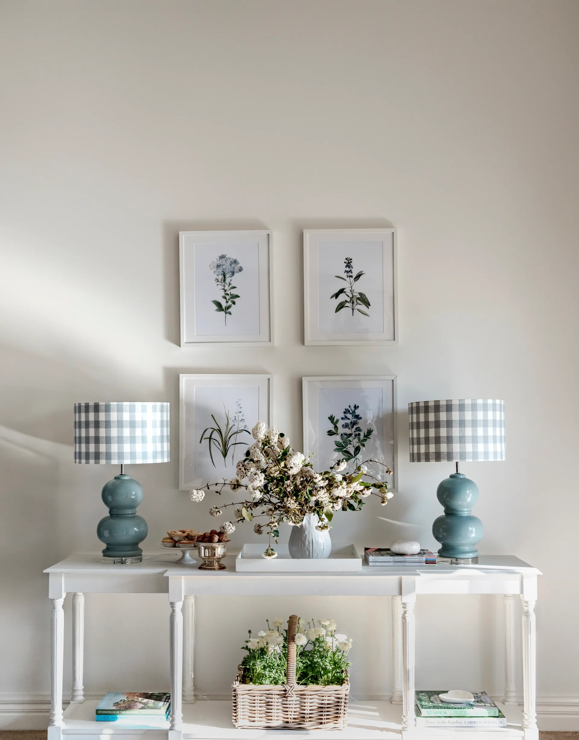 A Hamptons style white console with blue lamps under framed floral art.