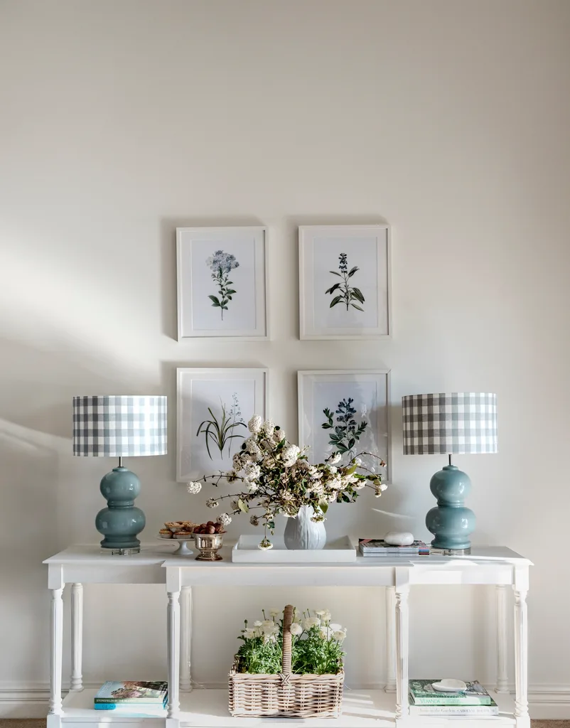 A Hamptons style white console with blue lamps under framed floral art.