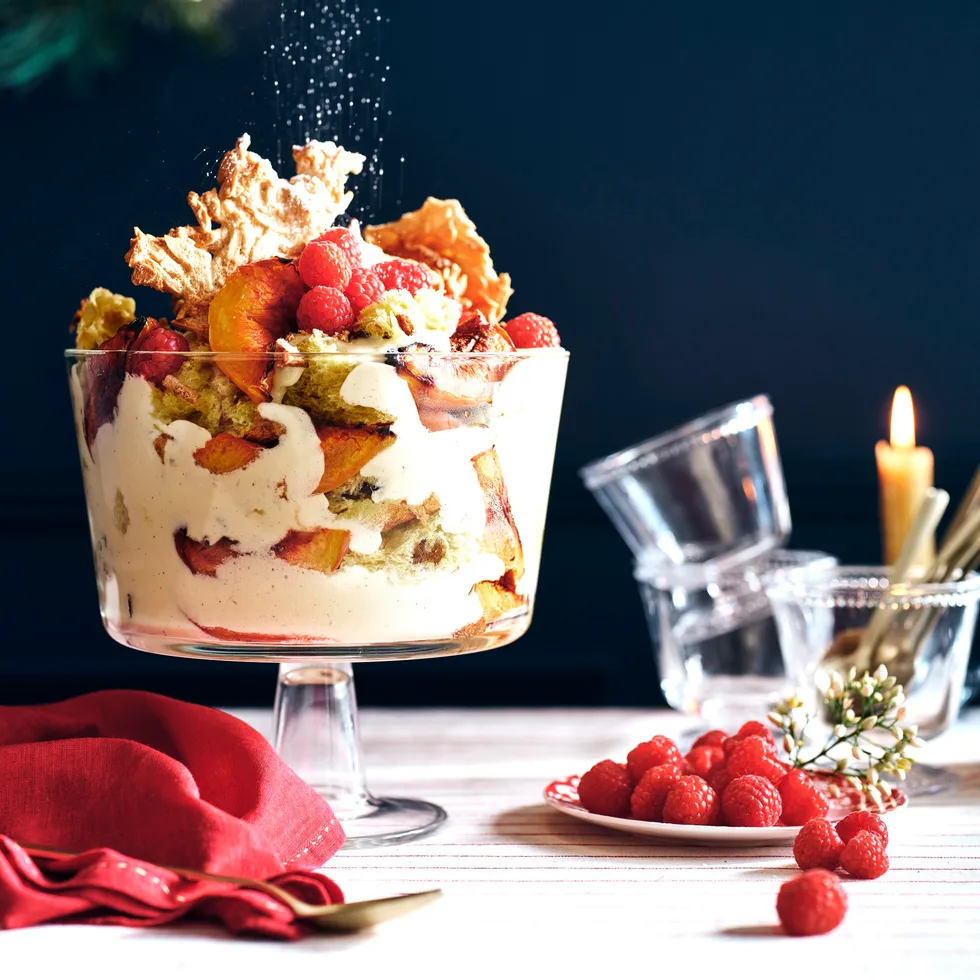 Fruit trifle in a trifle dish on a table decorated for Christmas.