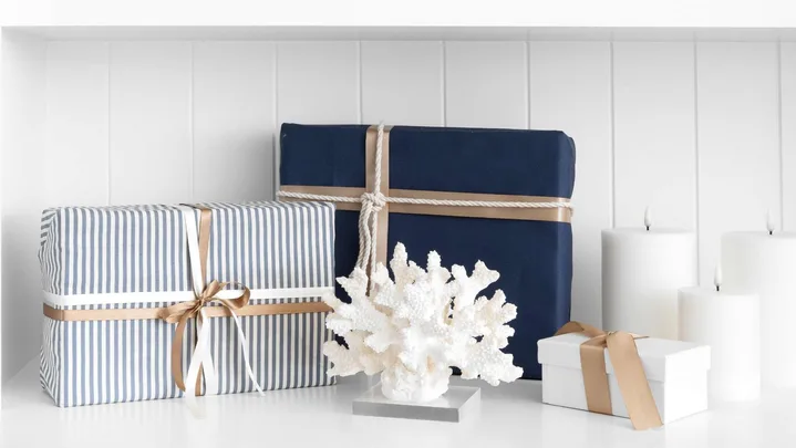 Nautical-themed gifts with blue and striped wrapping, coral decor, and candles on a white shelf.