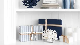 Nautical-themed gifts with blue and striped wrapping, coral decor, and candles on a white shelf.