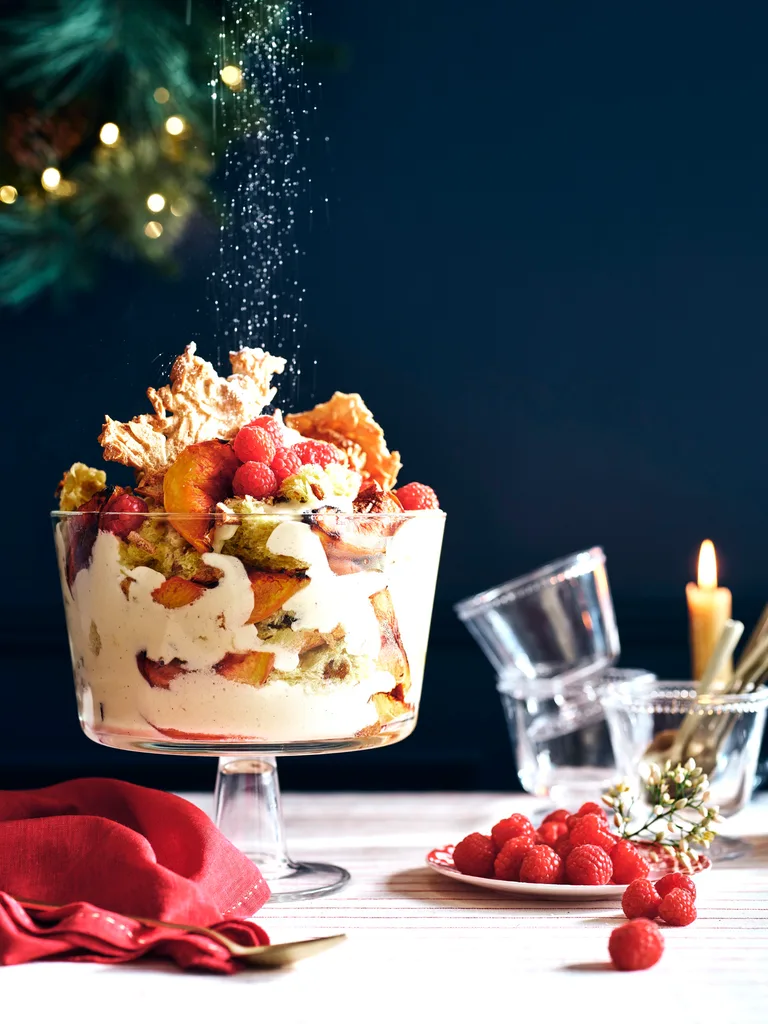 Christmas fruit trifle in a clear trifle dish on a table decorated according to a navy and red Christmas colour scheme.