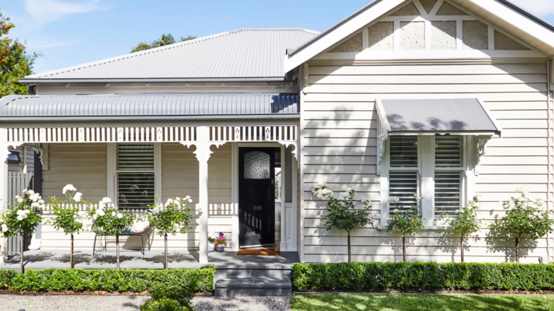 Alt text: "Charming beige cottage with porch, detailed trim, and manicured garden in front, under a blue sky."
