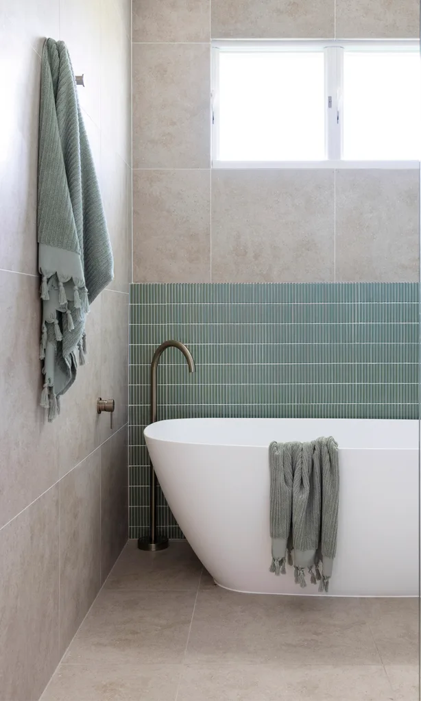 A minimalist bathroom with blue finger tiles and a freestanding bathtub.