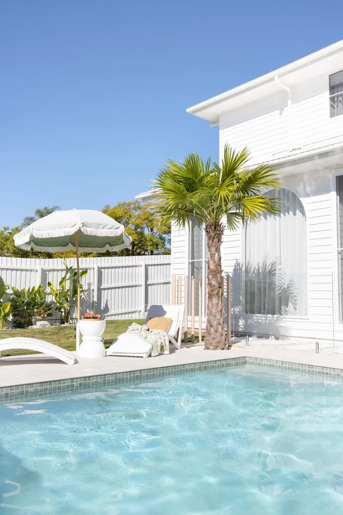 A resort-style pool with a palm tree and deck chairs.