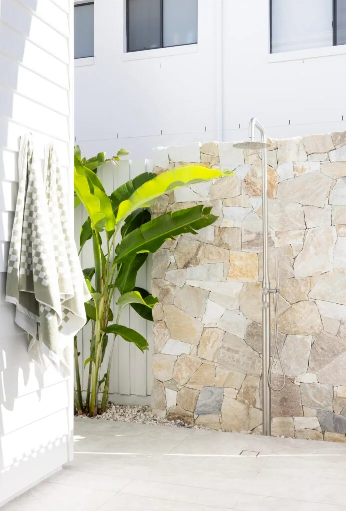 An outdoor shower beside a natural stone wall.