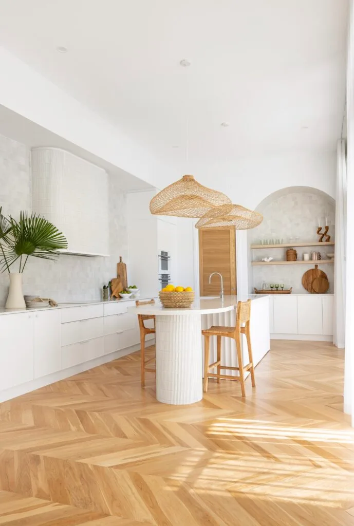 A white resort-style kitchen with oak flooring and hanging woven pendants.