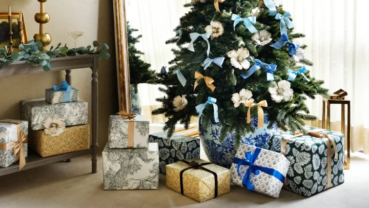 A decorated Christmas tree with floral ornaments and blue ribbons, surrounded by elegantly wrapped gift boxes.