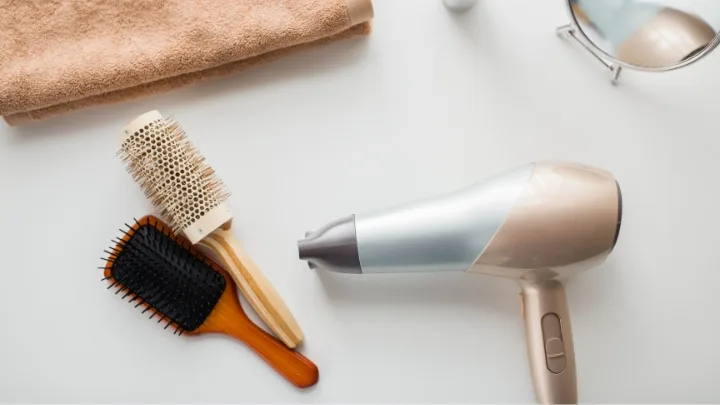 Hairdryer, round brush, paddle brush, towel, and mirror on a white surface.