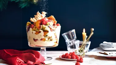 A trifle dessert with raspberries on a table set with candles and plates.