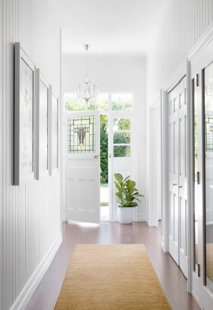 A white entry hall with a stained glass door and chandelier.