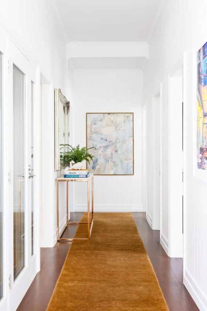 A white entry hall with an ochre runner and brass table.