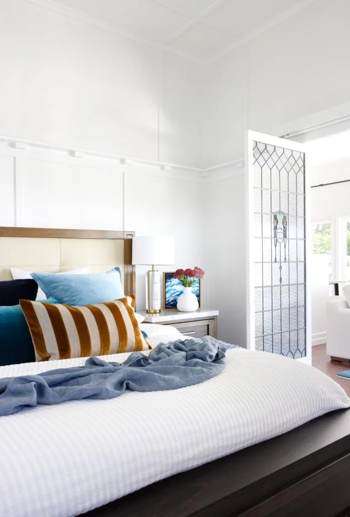 A white bedroom with stained glass doors and a white and timber bed.