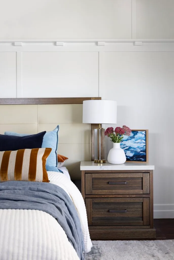 A timber and white topped side table beside a bed.