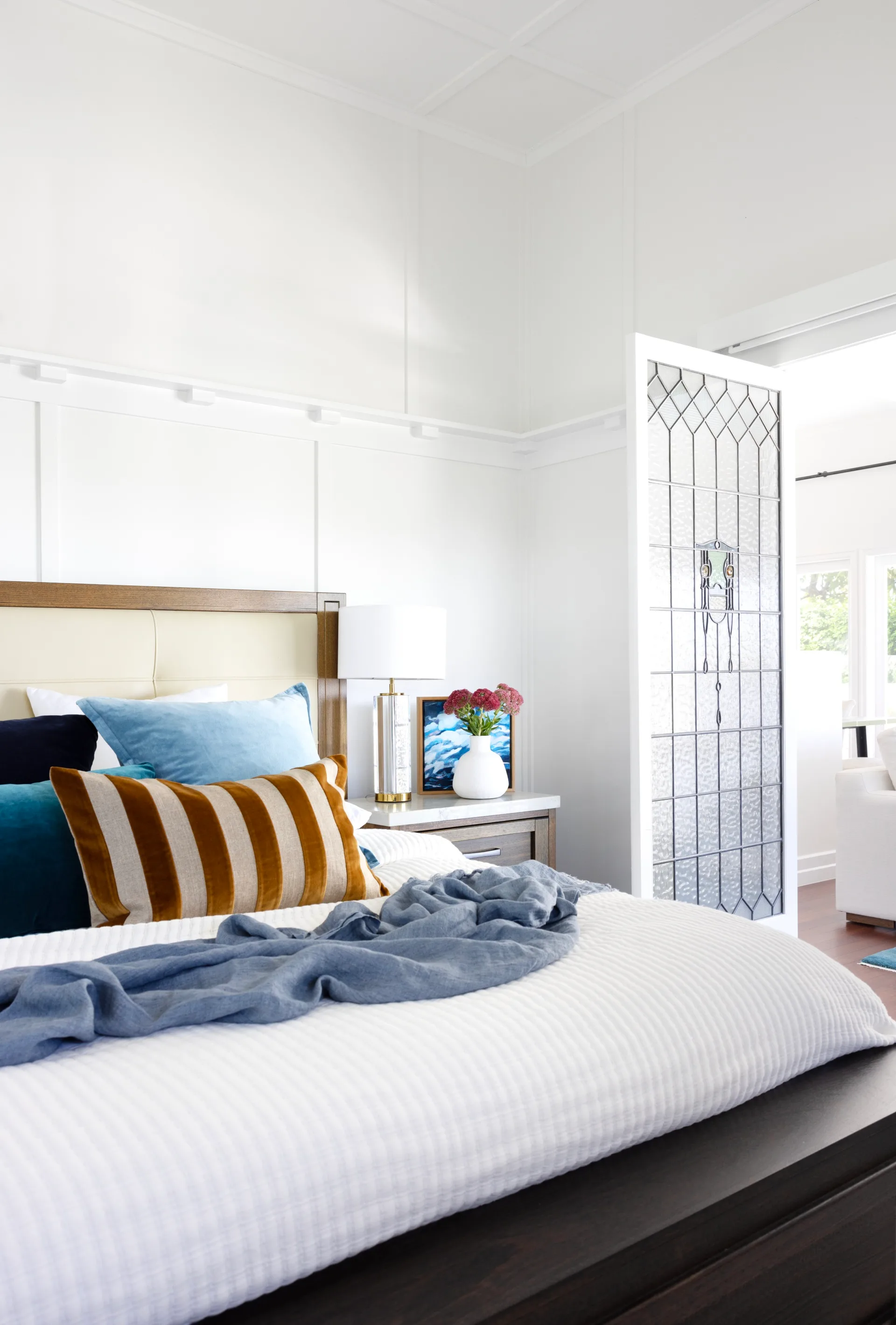 A white bedroom with stained glass doors and a white and timber bed.