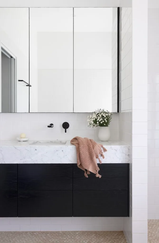 A black oak and white marble topped vanity below a mirrored cabinet.