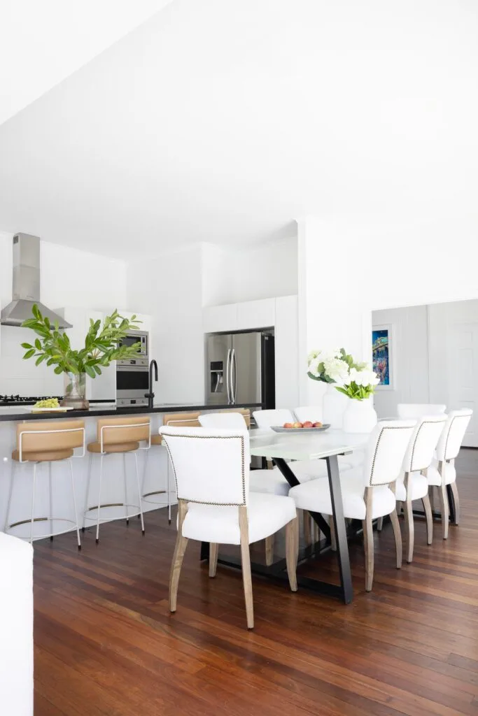 An all-white kitchen and dining area with timber hardwood floors.